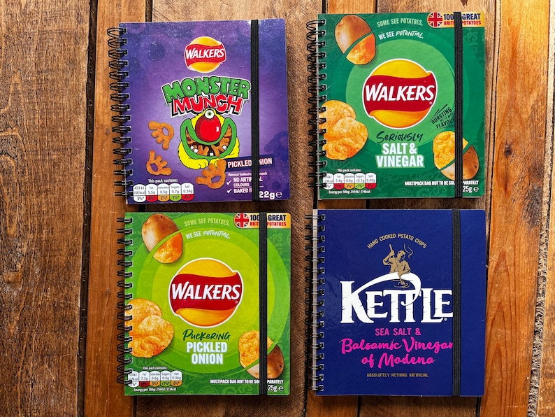 Puede incluir: Cuatro cuadernos de espiral diferentes con dise&ntilde;os de bolsas de patatas fritas. Los cuadernos presentan las marcas Walkers, Kettle y Monster Munch. Los cuadernos son todos azules, verdes y morados.