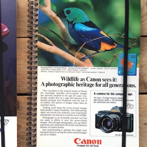 Könnte beinhalten: Ein Vintage-Notizbuch mit schwarzer Spiralbindung und einem farbenfrohen Bild eines siebenfarbigen Tangara-Vogels auf dem vorderen Umschlag. Das Notizbuch verfügt über einen schwarzen Gummibandverschluss und den Text "Wildlife as Canon sees it: A photographic heritage for all generations." Der hintere Umschlag zeigt eine Canon-Kamera und den Text "Canon Images for all time."