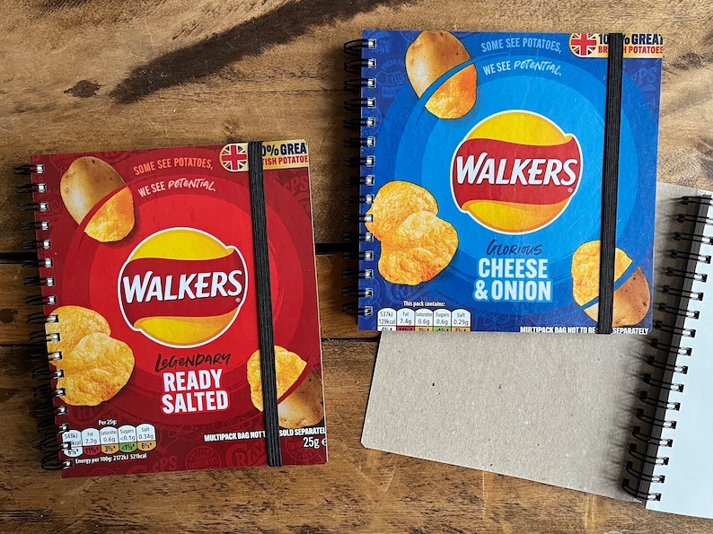 Puede incluir: Dos cuadernos de espiral con cubiertas que muestran envases de patatas fritas Walkers. Un cuaderno es rojo con el texto "Legendary Ready Salted" y el otro es azul con el texto "Glorious Cheese & Onion".