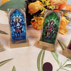 May include: Four small stained glass religious icons on gold stands. The icons feature images of angels with names "Saint Michael", "Saint Gabriel", "Saint Raphael", and "Saint Uriel".