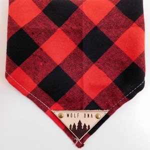 May include: Red and black checked bandana with a triangular leather patch that says "Wolf DNA" and has a silhouette of pine trees.