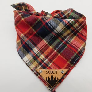 May include: Red, black and white plaid dog bandana with a wooden tag that says "SCOUT" and has a silhouette of pine trees.