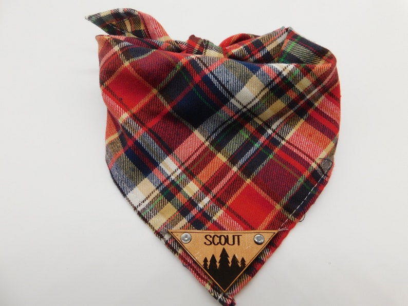 May include: Red, black and white plaid dog bandana with a wooden tag that says "SCOUT" and has a silhouette of pine trees.