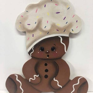 May include: A gingerbread man with a white icing hat decorated with colorful sprinkles. The gingerbread man is sitting with his legs crossed and has a brown body with white icing details.