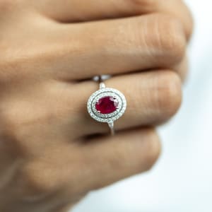 Peut inclure: Une bague en argent avec une pierre ovale rouge entourée d'un halo de petits diamants.