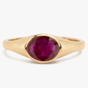 May include: A gold ring featuring a deep red oval ruby gemstone.