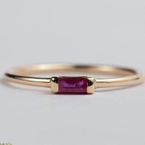May include: A delicate gold band ring with a single, rectangular ruby gemstone set in the center.