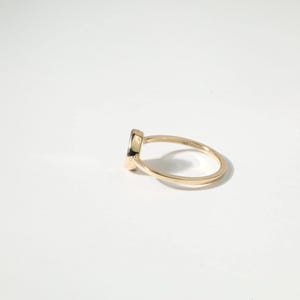 A gold ring with a small black gemstone is shown against a white background.