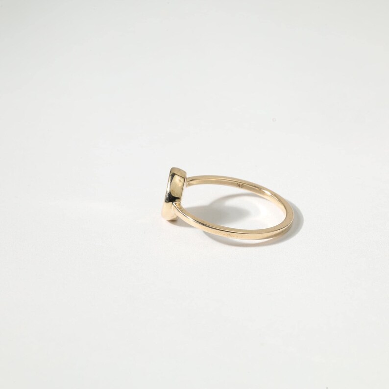 A gold ring with a small black gemstone is shown against a white background.