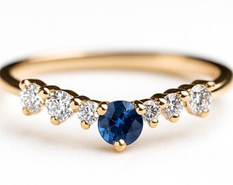 May include: A gold ring with a curved design, featuring a central round, deep blue gemstone, flanked by six smaller, clear gemstones. The ring's band is a thin, polished gold, creating a delicate and elegant appearance. The gemstones are set in a symmetrical pattern.