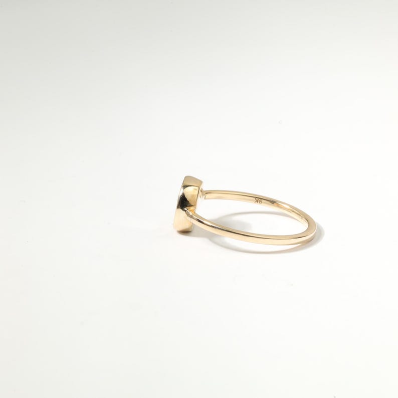 A gold ring with a small, round stone or gemstone is shown against a plain white background.