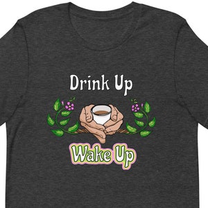 May include: Dark heather grey t-shirt with a white graphic of two hands holding a cup of coffee. The text "Drink Up" is above the graphic and "Wake Up" is below the graphic.