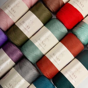 May include: A close-up of various colours of macrame cord, each spool labelled with the brand name "SENSY" and the cord thickness in millimetres. The cords are arranged in a circular pattern, with the brand labels facing outwards.