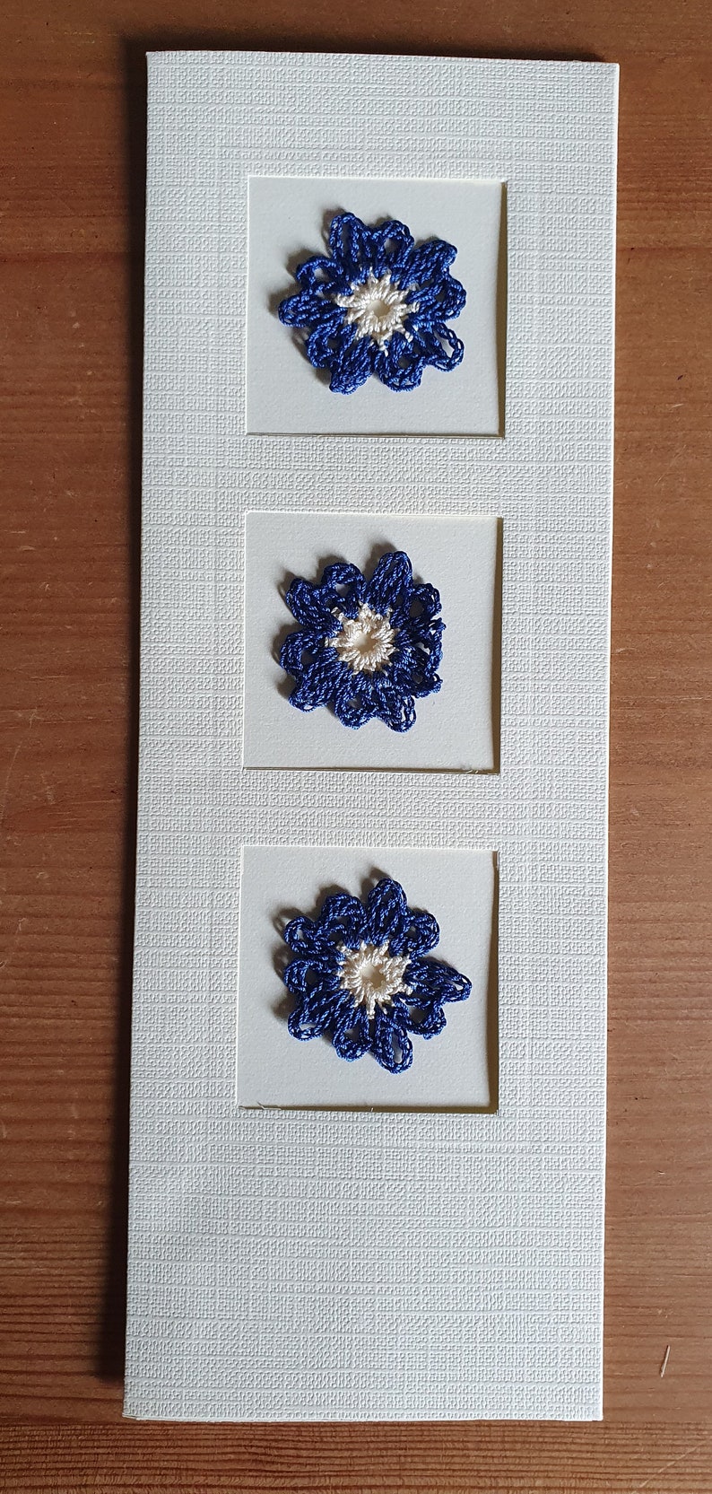 May include: A white card with three blue and white crocheted flowers in frames.