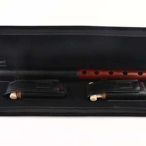 May include: A black carrying case with a zipper is open, revealing a wooden flute with a brown finish and six finger holes. Two smaller wooden pieces are also inside the case.