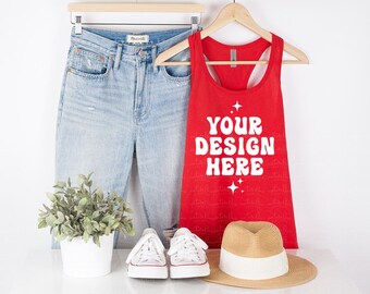 May include: A red vest top with the text "YOUR DESIGN HERE" is displayed with light blue jeans, white trainers, and a straw hat. A small potted plant is also present. The items are arranged on a white surface.