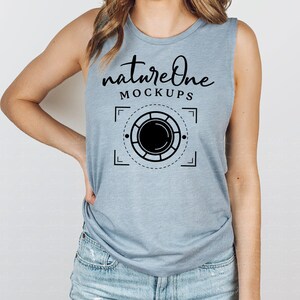 Peut inclure: Un débardeur bleu clair sans manches avec le texte "natureone MOCKUPS" et un graphique d'un objectif d'appareil photo à l'intérieur d'un cadre géométrique.