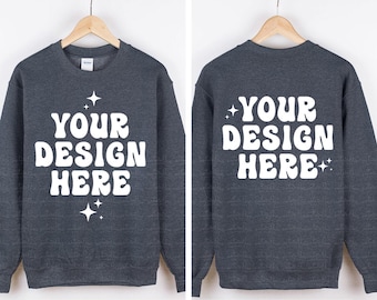 May include: A dark heather grey crewneck sweatshirt featuring the white text "YOUR DESIGN HERE" in a bold, wavy font. The design is accented with small four-pointed star graphics. The image displays both the front and back views of the garment.