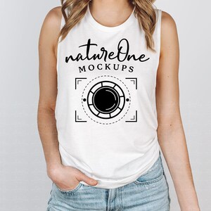 Peut inclure: Un débardeur blanc sans manches avec un motif graphique noir qui dit "natureone MOCKUPS" et un graphique de lentille d'appareil photo stylisé.