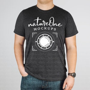 May include: A dark charcoal heather gray short-sleeve t-shirt featuring white screen-printed text that reads natureOne MOCKUPS above a circular graphic design with a central circle surrounded by a segmented ring and corner brackets.