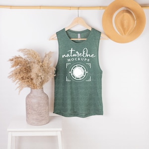 May include: A green sleeveless shirt with a white graphic that says "natureone MOCKUPS" and a circle design. The shirt is hanging on a wooden hanger against a white wall.