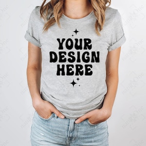 Puede incluir: Una camiseta gris jaspeado de manga corta con dobladillos, que presenta el texto negro YOUR DESIGN HERE en una fuente negrita y ondulada, centrado en el pecho, acompañado de cuatro pequeñas estrellas negras de cuatro puntas arriba y abajo.