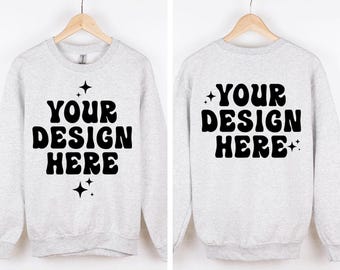 Puede incluir: Una sudadera gris claro de cuello redondo con el texto negro YOUR DESIGN HERE en una fuente negrita y ondulada, acentuada por pequeños iconos de estrellas de cuatro puntas. La imagen muestra las vistas frontal y trasera en perchas.