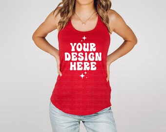Puede incluir: Una camiseta sin mangas roja con el texto blanco "YOUR DESIGN HERE" y estrellas. La camiseta se combina con vaqueros azules claros. Se ve un collar de oro. La imagen muestra un atuendo informal.