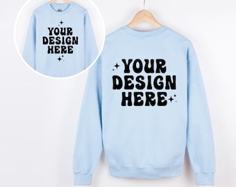 May include: A light blue crewneck sweatshirt featuring the black text YOUR DESIGN HERE in a bold, wavy font, accented by small four-pointed star icons. The design is displayed on both the front and back of the garment, shown on hangers.