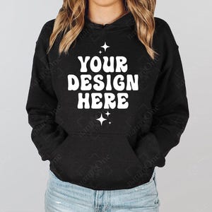 Op de afbeelding: Zwarte hoodie met de witte tekst "YOUR DESIGN HERE", met sterrenafbeeldingen. De hoodie heeft een voorzak en een capuchon met trekkoord. Het model draagt een blauwe spijkerbroek.