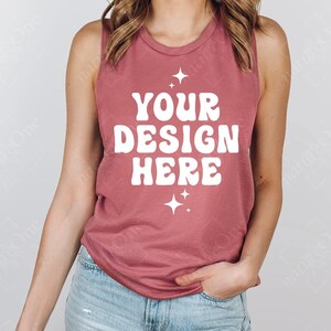 May include: A dusty rose tank top with the text "YOUR DESIGN HERE" in white, retro-style lettering. Two white starburst graphics are below the text. The model is wearing blue jeans.