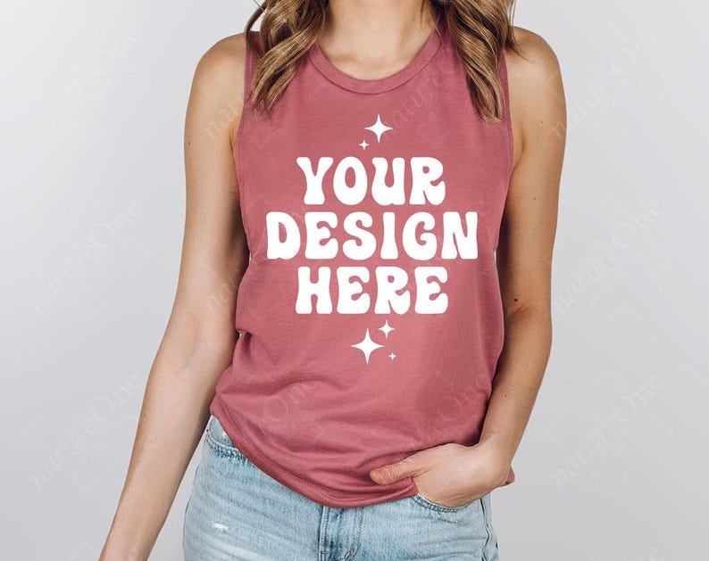 May include: A dusty rose tank top with the text "YOUR DESIGN HERE" in white, retro-style lettering. Two white starburst graphics are below the text. The model is wearing blue jeans.