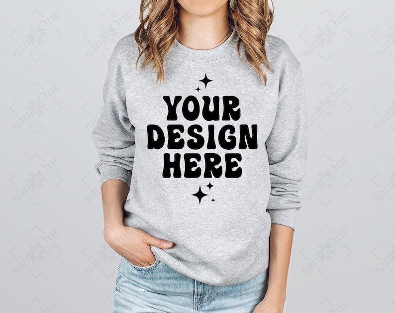 Puede incluir: Sudadera gris claro con el texto "YOUR DESIGN HERE" en negrita negra, con una fuente retro. El dise&ntilde;o est&aacute; flanqueado por dos gr&aacute;ficos de estrellas negras. La sudadera es de cuello redondo.