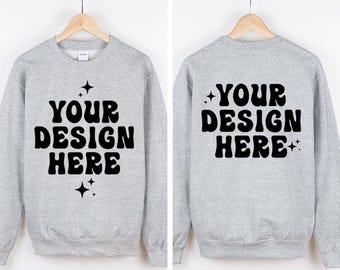 May include: A light gray crewneck sweatshirt featuring the black text "YOUR DESIGN HERE" in a wavy font, accented by small four-pointed star icons. The image displays both the front and back views of the garment, each hanging on a wooden hanger.