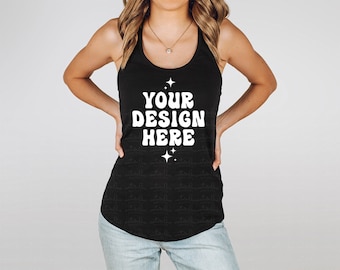 May include: A black racerback tank top featuring white text that reads YOUR DESIGN HERE, centered with a small four-pointed star graphic above and below the text. The garment has a scoop neckline and a curved hemline, worn with light blue jeans.