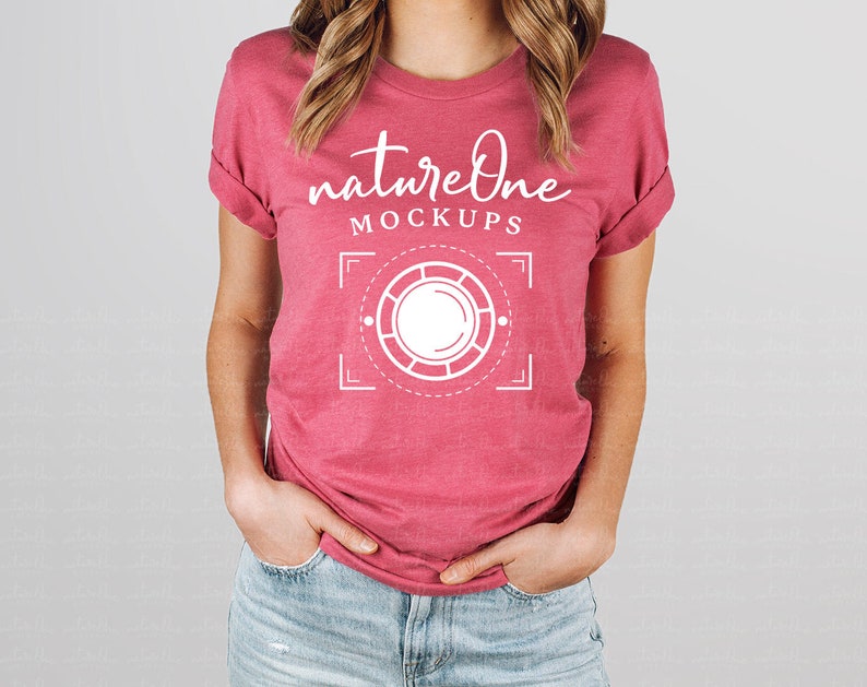May include: A heathered dark pink short-sleeve t-shirt featuring white text that reads natureOne MOCKUPS above a white graphic of a circular camera lens frame with corner brackets and dashed lines centered on the chest area of the garment.