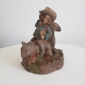 May include: A detailed figurine of a man in a cowboy hat riding a squirrel. The man wears a blue jacket and holds a small object. The base of the figurine has the words "Buffalo Bill" and the year "1983" inscribed.
