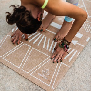May include: A brown yoga mat with white geometric designs and the text "SEEMA YOGA" printed on it. A person is doing a yoga pose on the mat.