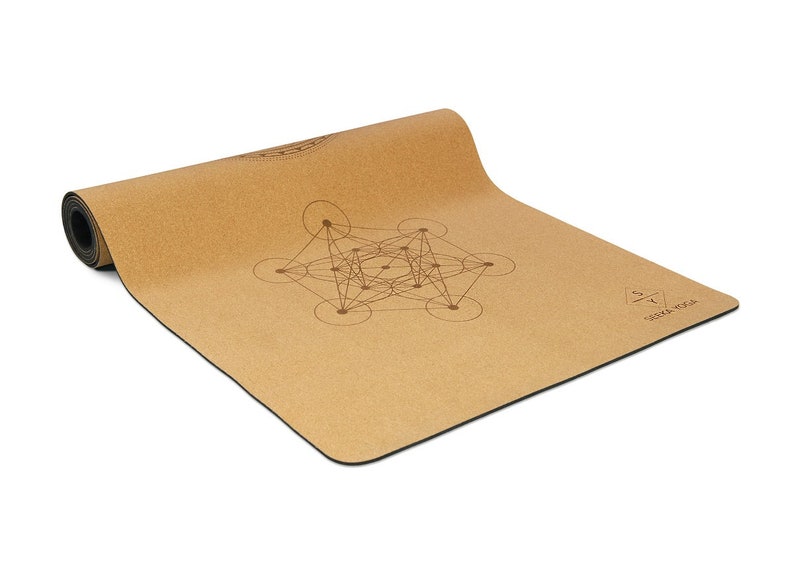 May include: A brown cork yoga mat with a geometric design printed on it. The mat is rolled up and has a black edge. The text "Soma Yoga" is printed on the mat.