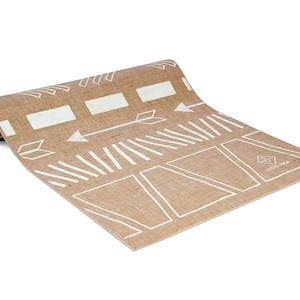 May include: A rolled up brown yoga mat with a white geometric pattern and the word "Manduka" printed on the bottom right corner.
