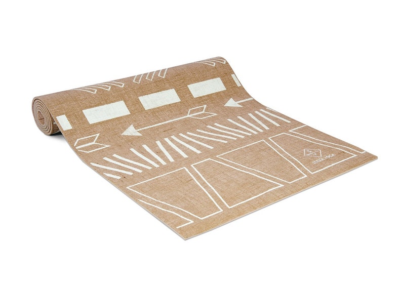 May include: A rolled up brown yoga mat with a white geometric pattern and the word "Manduka" printed on the bottom right corner.