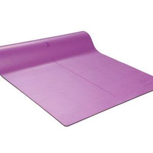 Pu&ograve; includere: Un tappetino da yoga viola con una superficie leggermente testurizzata. Il tappetino &egrave; arrotolato e ha un cinturino nero.