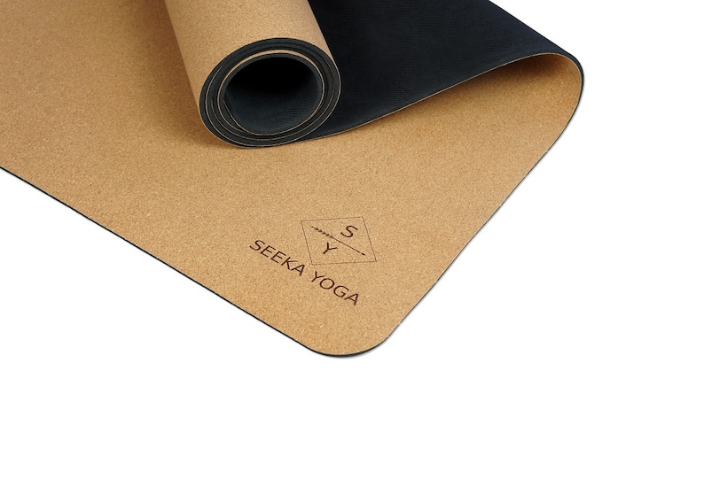 May include: A rolled up cork yoga mat with a black underside. The mat has the text "SEEKA YOGA" and a logo with the letters "S" and "Y" printed on it.