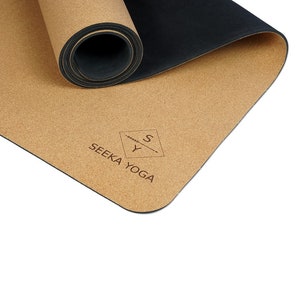 Op de afbeelding: Een opgerolde kurken yogamat met een zwarte onderkant. De mat heeft de tekst "SEEKA YOGA" en een logo met de letters "S" en "Y" erop gedrukt.