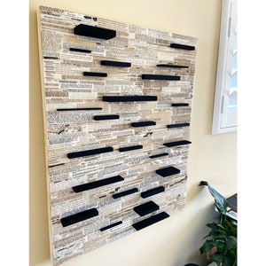 May include: A wall art piece made of a wood panel covered in a vintage newspaper print. The panel has multiple black floating shelves attached to it in a staggered pattern.