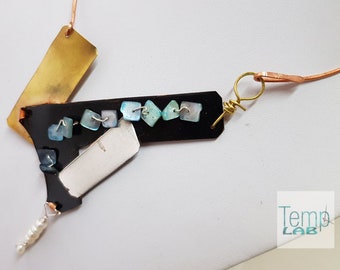 May include: A necklace featuring a black geometric pendant adorned with small light blue square beads, a rectangular brass plate, a silver-toned blade-like element, and a small white pearl dangle, all suspended from a copper wire with the text Temp LAB.