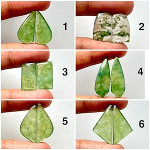 Puede incluir: Seis pares de piedras preciosas pulidas en varias formas y tonos verdes. Las piedras se sostienen entre los dedos, mostrando sus diferentes cortes: corazón, rectangular, lágrima y formas geométricas. Las piedras tienen una calidad translúcida.