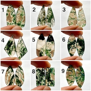 Puede incluir: Una colección de nueve pares de cabujones de ágata musgosa en varias formas. Las piedras preciosas presentan patrones verdes, marrones y blancos. Cada par se sostiene entre los dedos, mostrando las vetas y variaciones de color únicas.