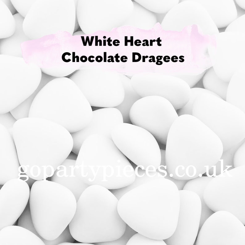 Op de afbeelding: Close-up van witte hartvormige chocoladedragees. De snoepjes zijn verspreid, waardoor een textuurpatroon ontstaat. De tekst "White Heart Chocolate Dragees" wordt in het midden bovenaan weergegeven.