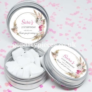 May include: Silver favor tins with white lids and personalized labels. The labels feature a floral design with pink and gold accents. The text on the label reads "Sara's 21st Birthday 04th July 2022 Thank you for coming x".